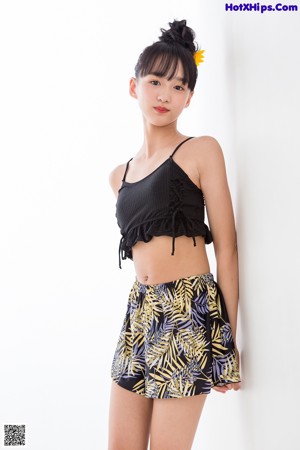 A woman leaning against a white wall with her hands on her hips.