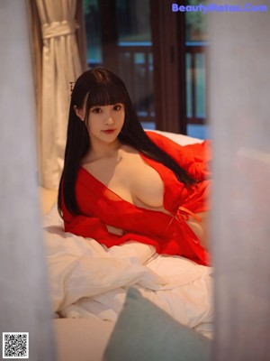 A woman in a red robe sitting on a window sill.