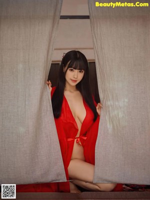A woman in a red dress sitting on a bed.