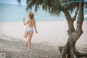 A woman in a bikini sitting under a palm tree on the beach.