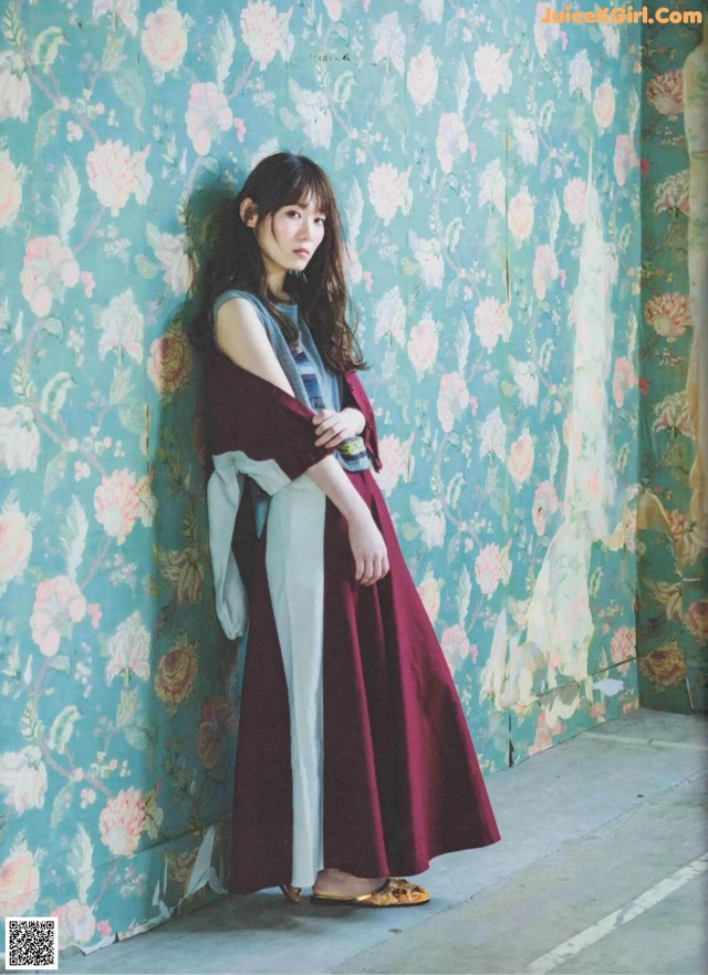 A woman standing in front of a floral wallpaper.