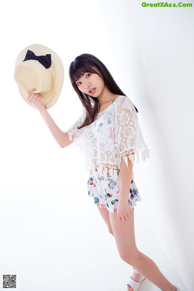 A woman in a white top and shorts holding a straw hat.