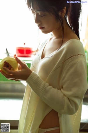 A woman in a white sweater is holding an apple.