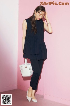 A woman sitting on a pink wall wearing a black dress.