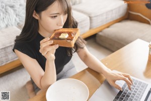 A woman sitting at a table with a laptop and a plate of toast.