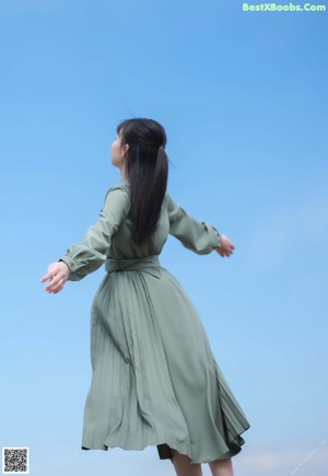 A woman in a green dress sitting on a rock by the water.