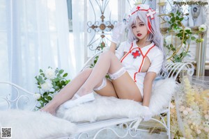 A woman in a white nurse outfit sitting on a bed.