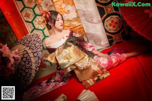A woman in a kimono sitting on a red couch holding a fan.
