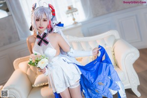 A woman in a white dress sitting on a bed.