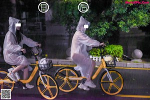 A couple of people riding bikes down a street in the rain.