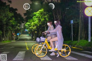 A couple of people riding bikes down a street in the rain.