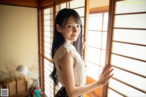 A woman with long black hair leaning against a wall.