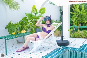 A woman in a purple bikini sitting on a lounge chair by a pool.