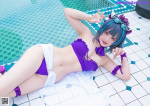 A woman in a purple bikini sitting on the edge of a pool.