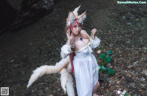 A woman in a white dress sitting on a rock next to a white wolf.