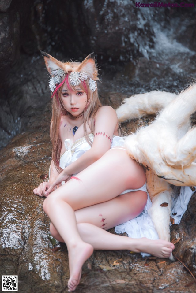 A woman in a white dress sitting on a rock next to a white wolf.